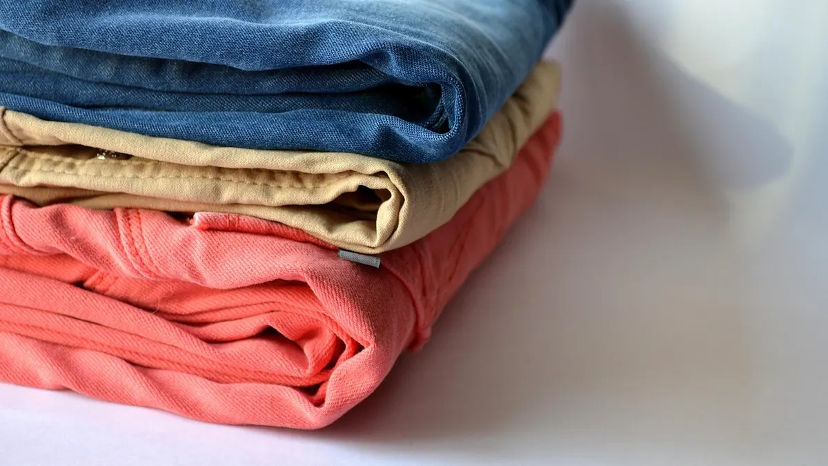Pilha de jeans e roupas dobradas sobre fundo claro